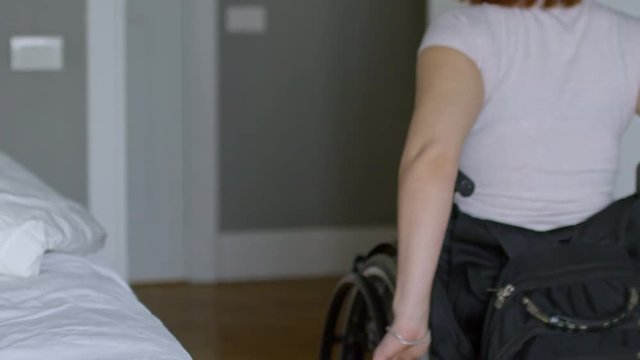 Tilt up of paraplegic woman in wheelchair leaving bedroom in morning