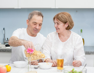 Senior man pours a dry breakfast to his wife in the kitchen