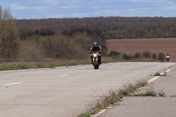 Obraz premium Male motorcyclist at the wheel of a racing motorcycle on a high-speed empty road. with pleasure passing an empty road to travel by motorcycle. Place for text, extreme sport, freedom concept