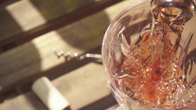 Slow motion rose wine from a bottle neck pours in a crystal glass on a wooden table