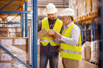 Large scale trade. Delighted nice man holing a box while standing with his colleague in the warehouse