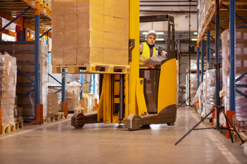 Fototapeta na wymiar Technical automation. Nice serious man carrying boxes while using a driving a special machine vehicle