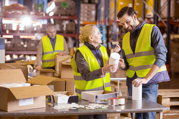 Wholesale production. Nice warehouse worker smiling and looking at each other while putting labels on the products 