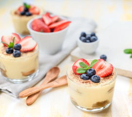 homemade, exquisite dessert tiramisu in glasses decorated with strawberry, blueberry, mint on white wooden table