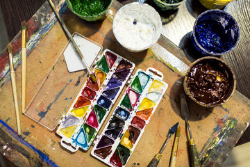 top view of poster paints and watercolor paints on wooden table in workshop