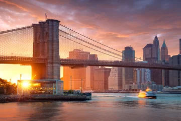 Fototapeten Berühmte Brooklyn Bridge in New York City mit Bankenviertel - Downtown Manhattan im Hintergrund. Sightseeing-Boot auf dem East River und schöner Sonnenuntergang über Janes Karussell. © dell
