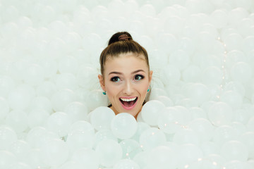 Happy beautiful woman lays surrounded by white plastic balls