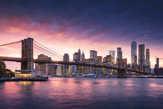 Famous Brooklyn Bridge in New York City with financial district - downtown Manhattan in background. Sightseeing boat on the East River and beautiful sunset over Jane's Carousel. © dell