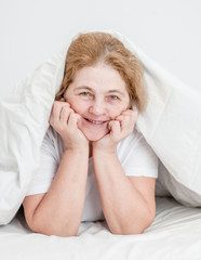 Happy senior woman lying uder blanket