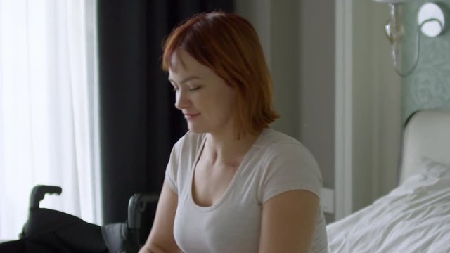 Medium shot of happy paraplegic woman waking up and getting into wheelchair, then riding away to make breakfast