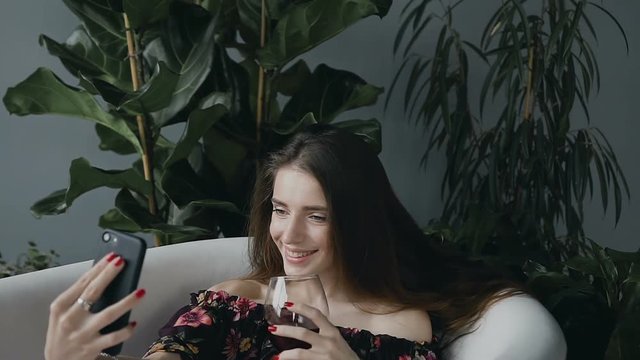 A attractive girl with long hair makes a photo of sephi on her phone with a glass of red wine in a warm milk bath. Body care. Technologies