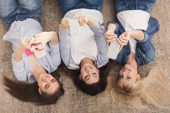 Happy girls lying on floor and using smartphones, top view