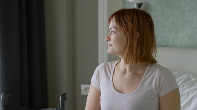 Medium shot of paraplegic woman sitting on bed and stretching in morning, then getting into wheelchair, then riding away