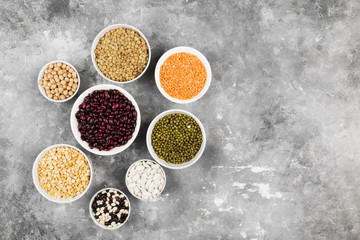 Assortment of beans (red lentil, green lentil, chickpea, peas, red beans, white beans, mix beans, mung bean) on gray background. Top view, copy space. Food background