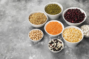 Obraz na płótnie Canvas Assortment of beans (red lentil, green lentil, chickpea, peas, red beans, white beans, mix beans, mung bean) on gray background. Copy space. Food background