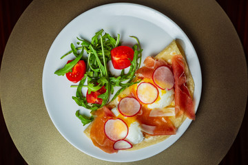Eggs Benedict with hamoon, radish, cherry tomatoes and Olandes sauce on a white plate