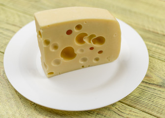 A piece of cheese with holes  on a white plate.