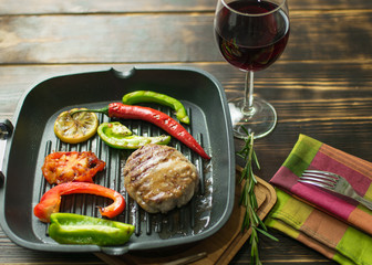 Frying pan with a meatball and vegetables and a glass of wine.