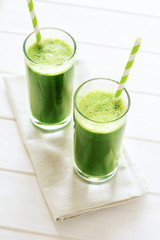 Healthy green smoothie made from spinach, apple and cucumber in a jars with red straw on white wooden table