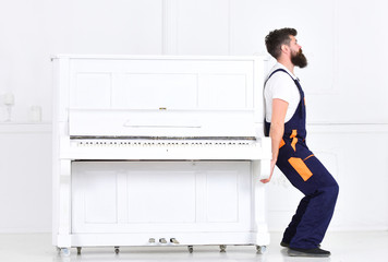 Handsome bearded strong man lifting old wooden piano with open keyboard isolated on white background. Side view handsome worker trying to move heavy thing © be free