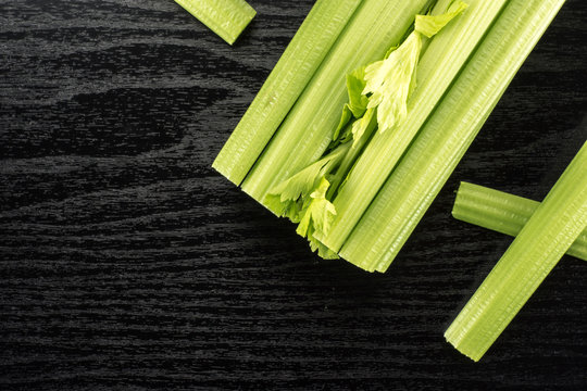 Fresh green celery with three sticks isolated on black wooden background.