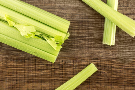 One fresh green celery with three sticks isolated on wooden background.