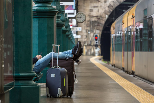 Passenger with suitcase is waiting for train on railway station.Delayed train concept.