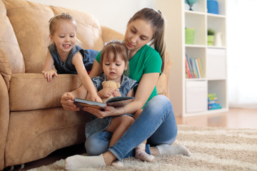 pretty young mother reading a book to her kids daughters