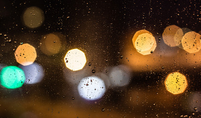 The background with the city lights at night with water drops on glass
