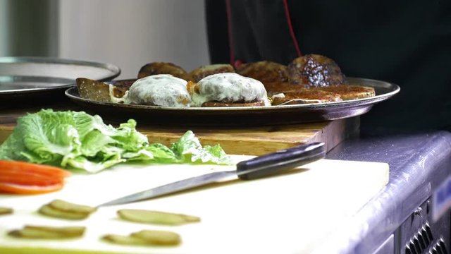 Hands of chief on commercial kitchen serves burgers on the plate - inside the restaurant
