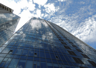 Glass surface of front part of city skyscraper with sky reflection in windows