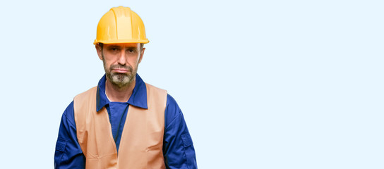 Senior engineer man, construction worker with sleepy expression, being overworked and tired isolated over blue background