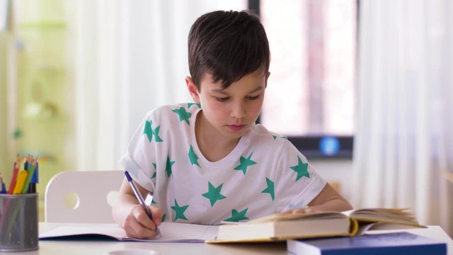 education, childhood and people concept - boy writing to notebook at home