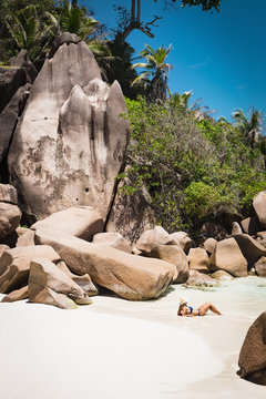 Side view of mid adult woman in bikini relaxing at beach, Island of La Digue, Seychelles