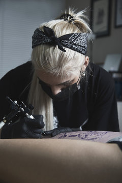 Artist wearing mask tattooing on customer's leg at art studio