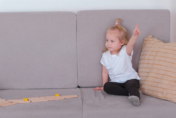 Naklejka premium Little charming girl sitting on the sofa talking and playing wood blocks.