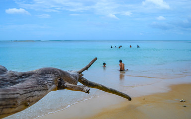 Scene of people playing in blue sea and blue sky through large timber phuket thailand.