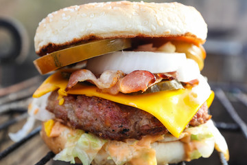 Homemade Burger with meat, bacon, cheese, tomatoes and onions which lies on the grill in the background of nature