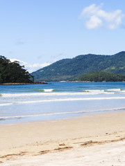 Beach in sunny day, with island and hills with forest in the background.