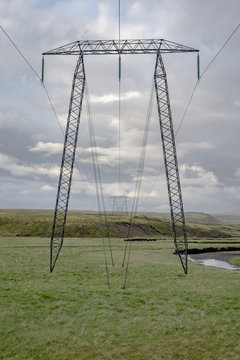 Row of electricity pylons on green field against cloudy sky, Highlands, Iceland