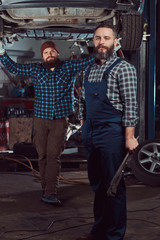 Obraz na płótnie Canvas Two bearded brutal mechanics repair a car on a lift in the garage. 