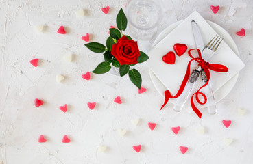 Table decoration for wedding or Valentine's Day, table setting with red ribbon, roses, knife and fork ring on white concrete background. Top view, overhead, flat lay