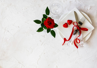 Table decoration for wedding or Valentine's Day, table setting with red ribbon, roses, knife and fork ring on white concrete background. Top view, overhead, flat lay