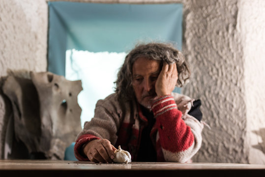 Poor man with gray hair looking at a bulb of fresh garlic