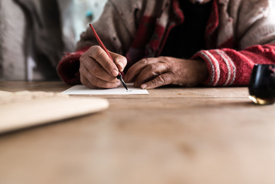 Old man with dirty hands writing a letter using a nib pen and ink