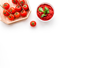 Tomato sauce in bowl with green basil near cherry tomatoes on white background top view copy space