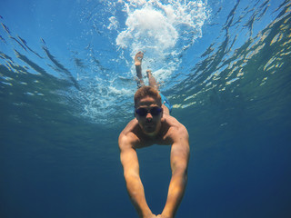 Underwater photo of a young muscular man diving in the turquoise exotic sea and taking a selfie...