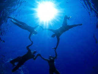 Underwater image of four playful friends enjoying holidays in the sea, holdings hands together and making star or circle.