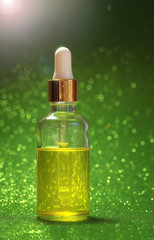 bright Golden cosmetic oil for beauty is in a transparent bottle with eye dropper brilliant green festive background Sunny