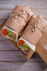 Fototapeta na wymiar Homemade tasty burrito with tuna fish, cucumber, avocado and carrot. Tuna wraps on wooden background. vertical, overhead